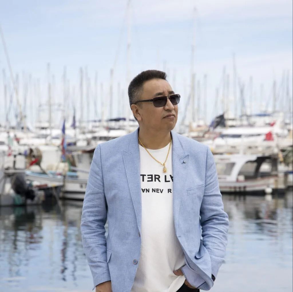 Founder Marcel posing to the right, wearing sunglasses, a white shirt with a blue colbert. In the background you can see variety of boats as this photo was taken on a dock.