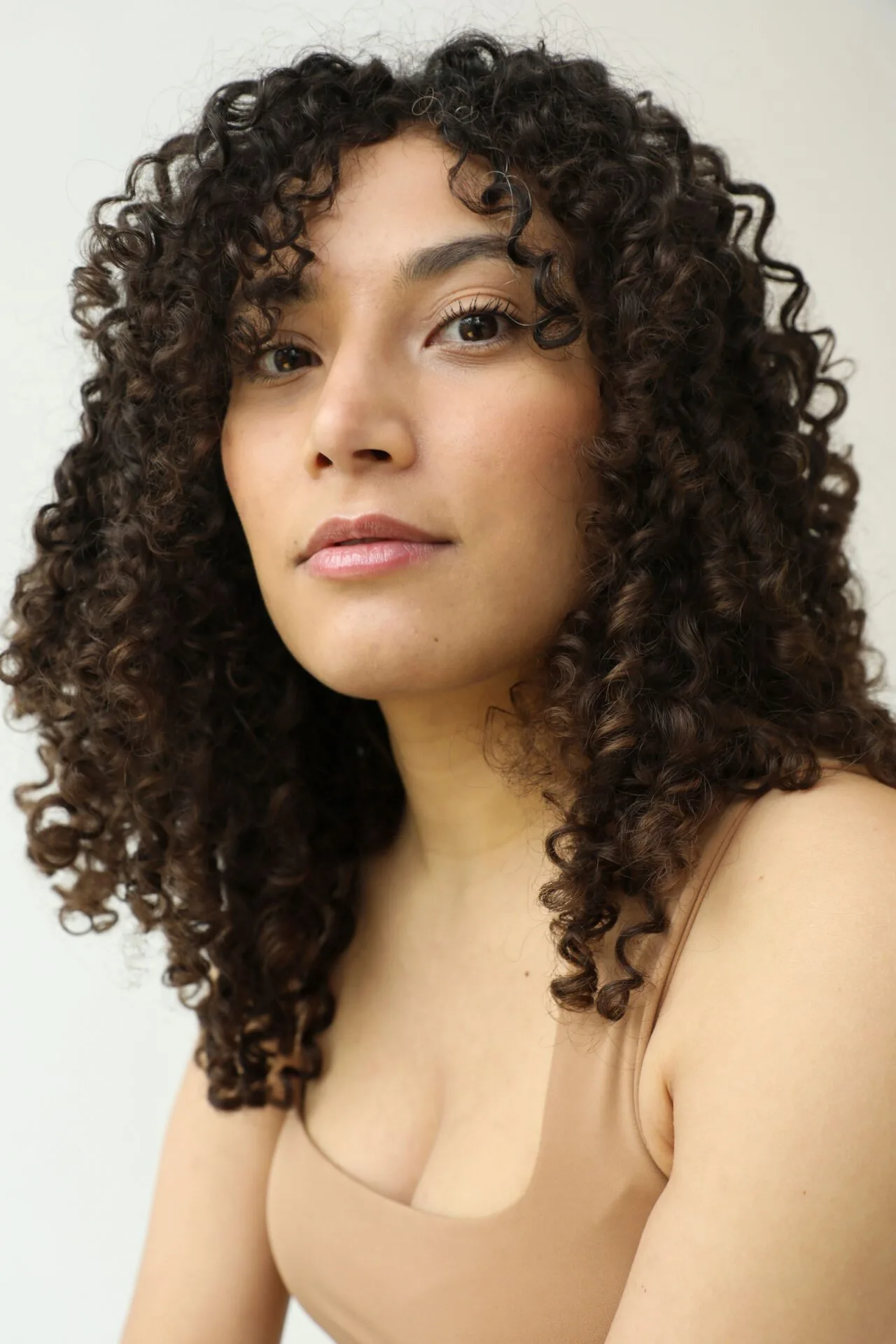 Headshot of a female model looking into the camera with curly brown hair and a brown top.